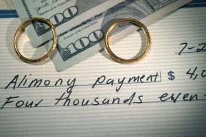 two wedding bands on top off two hundred dollar bills and a check that says alimony payment symbolizing St. Louis alimony and spousal support payments 